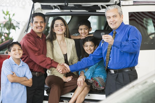 Hispanic car salesman handing car keys to family