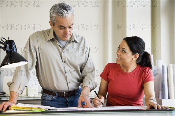 Hispanic male and female architects looking at blueprints