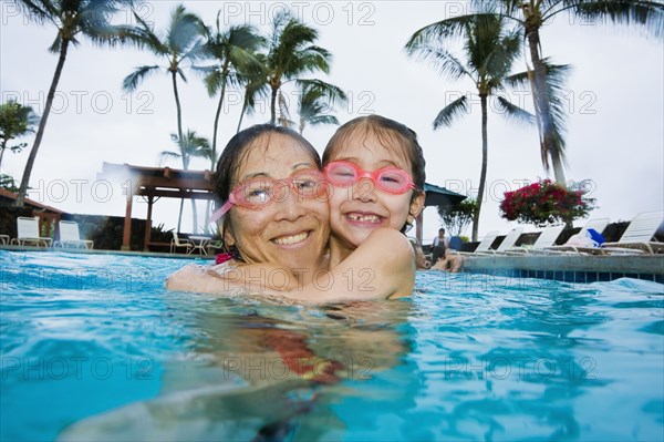 Asian mother and daughter hugging in swimming pool