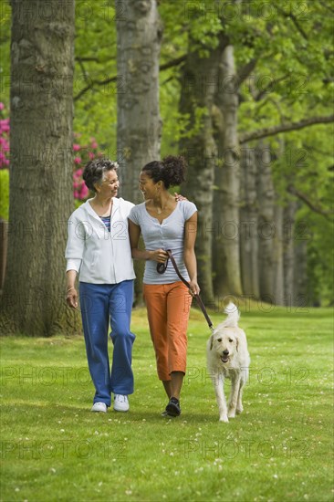 African American mother and adult daughter walking dog