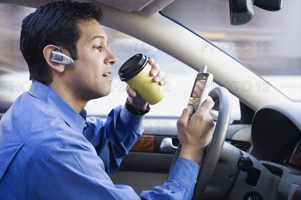 Hispanic businessman using cell phone drinking coffee and driving