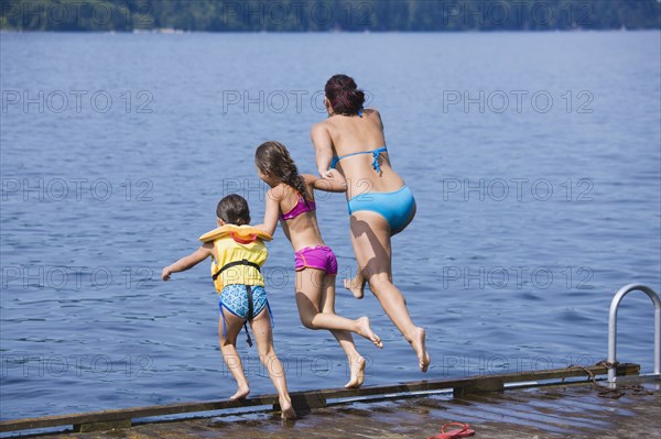 Mother and daughters jumping into lake