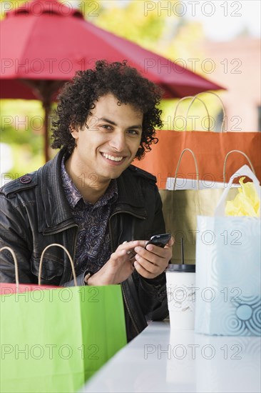 Middle Eastern man with shopping bags text messaging on cell phone