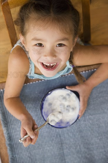 Mixed race young girl eating yogurt with spoon