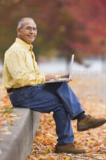 Hispanic man using laptop outdoors in autumn