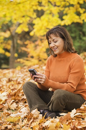 Hispanic woman using cell phone outdoors in autumn