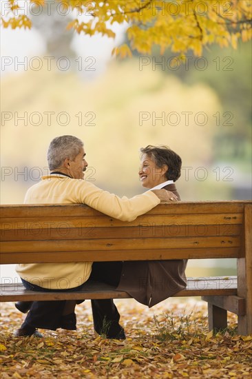 African couple sitting on park bench in autumn