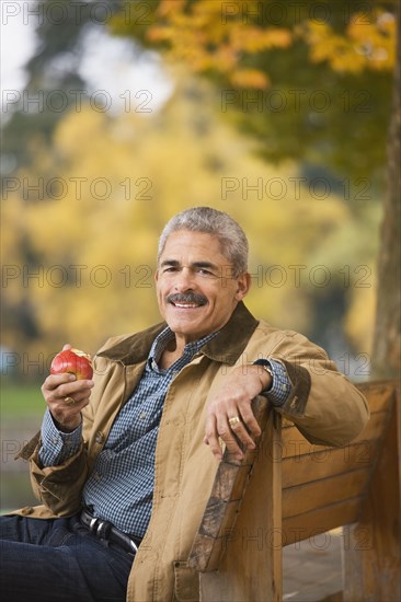 African man eating apple on park bench