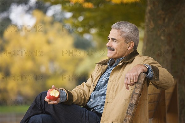 African man eating apple on park bench