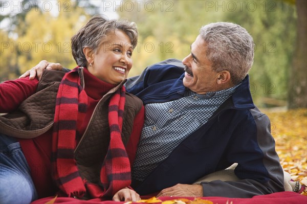 African couple laying on blanket among autumn leaves