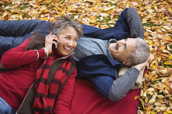 African couple laying on blanket in autumn with cell phone