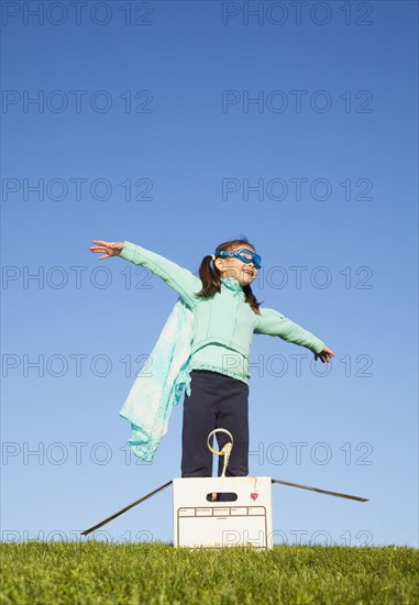 Mixed race girl wearing cape and standing in box