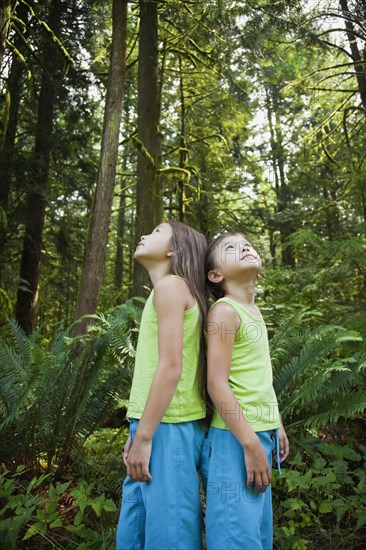 Mixed race girls standing back to back in forest