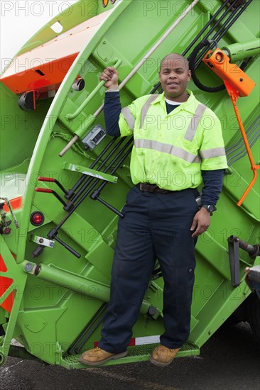 Black man riding on back of garbage truck