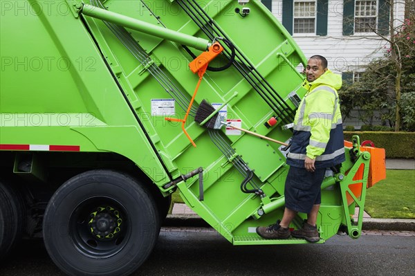 Pacific Islander man riding on garbage truck