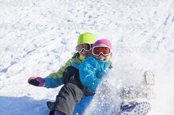 Mixed race girls sledding in snow