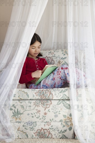 Mixed race girl reading on sofa