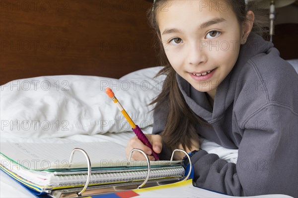 Mixed race girl doing homework on bed