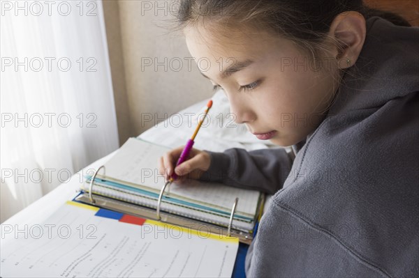 Mixed race girl doing homework on bed