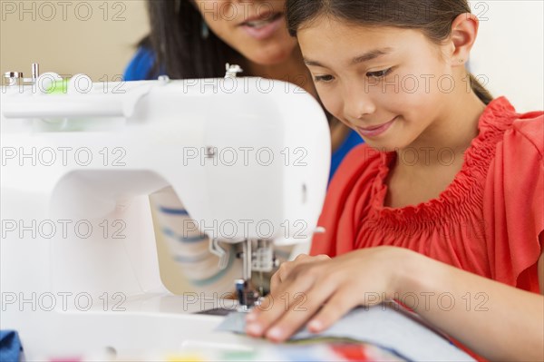 Mother teaching girl to use sewing machine