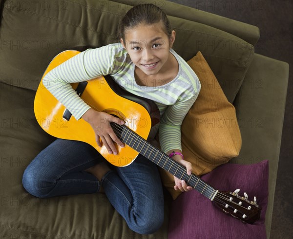 Mixed race girl practicing guitar on sofa
