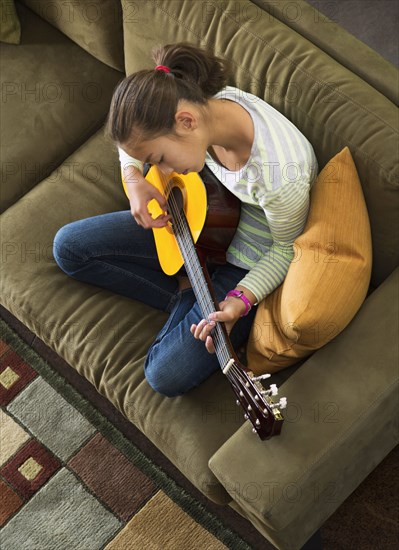 Mixed race girl practicing guitar on sofa