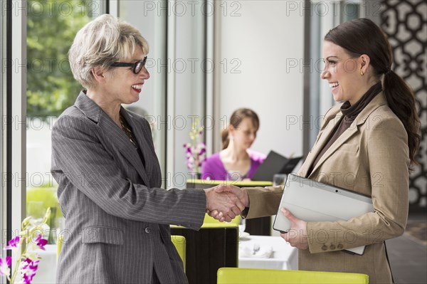 Caucasian businesswomen shaking hands in restaurant