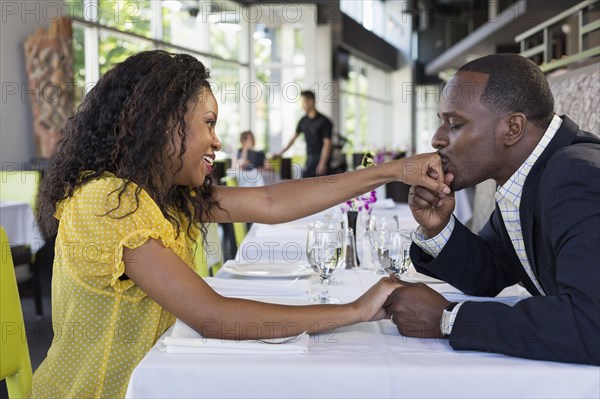 African American man kissing girlfriend's hand in restaurant