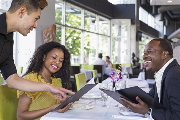 Waiter explaining menu to couple in restaurant