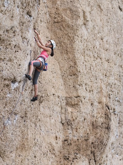 Mixed race girl climbing steep cliff