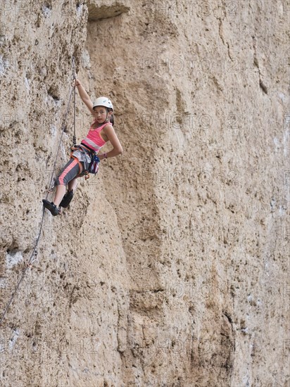 Mixed race girl climbing steep cliff