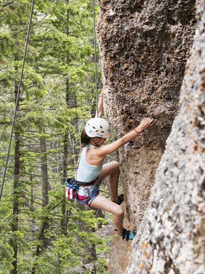 Mixed race girl climbing steep cliff