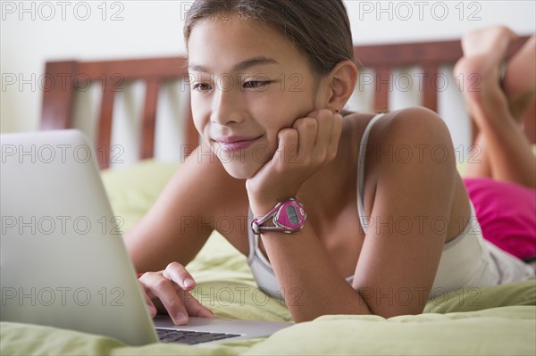 Mixed race girl using laptop on bed
