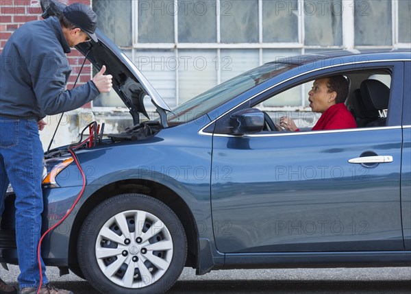 Mechanic jumping battery for woman in car