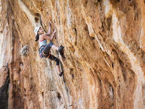 Mixed race girl climbing rock wall