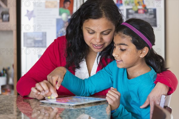 Indian mother and daughter using digital tablet at counter