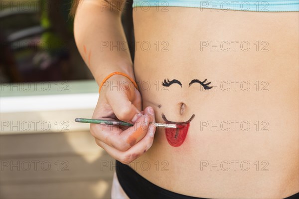 Mixed race girl painting face on stomach