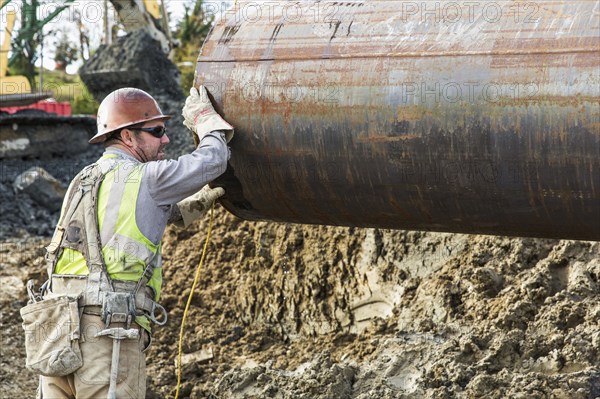 Caucasian worker hauling pipe at construction site