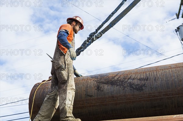 Caucasian worker hauling pipe at construction site