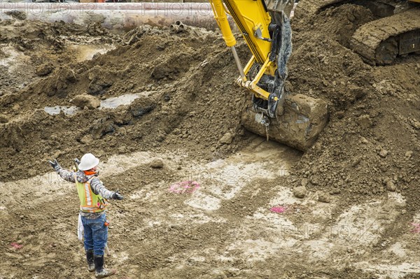 Caucasian worker directing digger at construction site