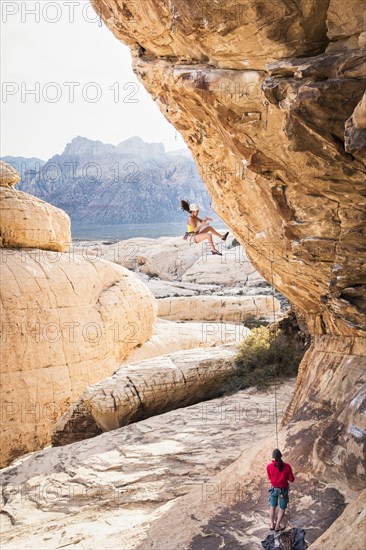 Mother belaying daughter rock climbing on cliff