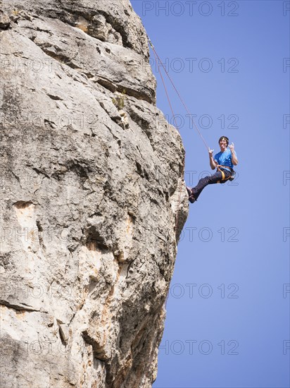 Caucasian man climbing rock gesturing with tongue out