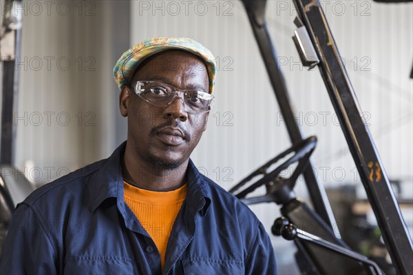 Serious Black worker posing near forklift in factory