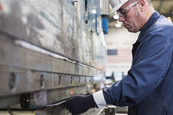 Hispanic worker fabricating metal in factory