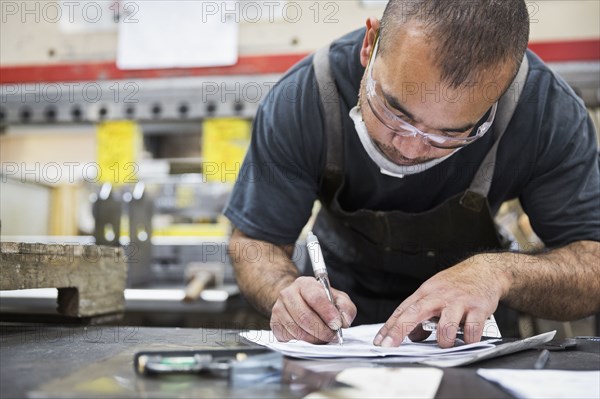 Hispanic worker writing on paperwork in factory