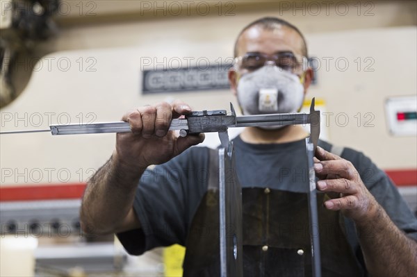 Hispanic worker measuring metal with caliper in factory