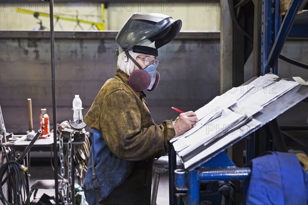 Asian worker wearing mask writing on paperwork in factory