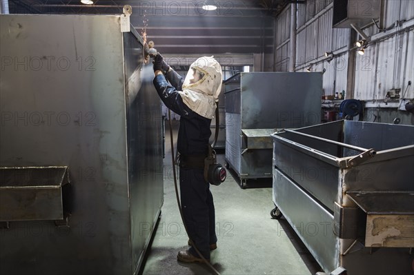 Caucasian worker grinding metal container in factory