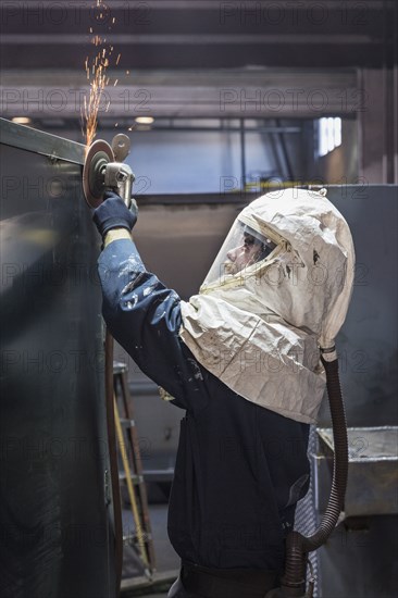 Caucasian worker grinding metal container in factory