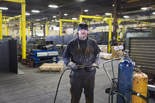 Caucasian welder posing with blowtorch in factory